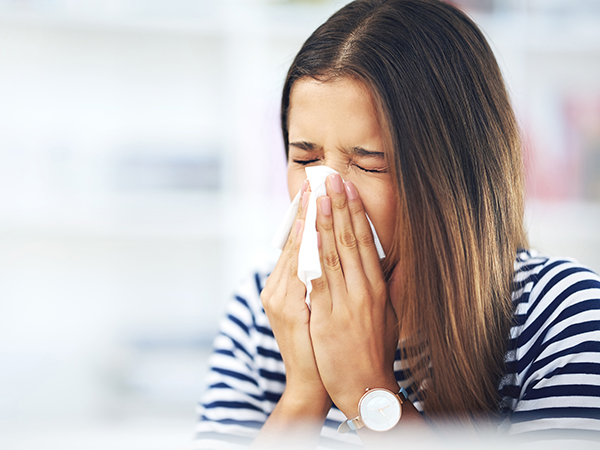 Its allergy season again. Shot of a young woman with allergies sneezing into a tissue at home.